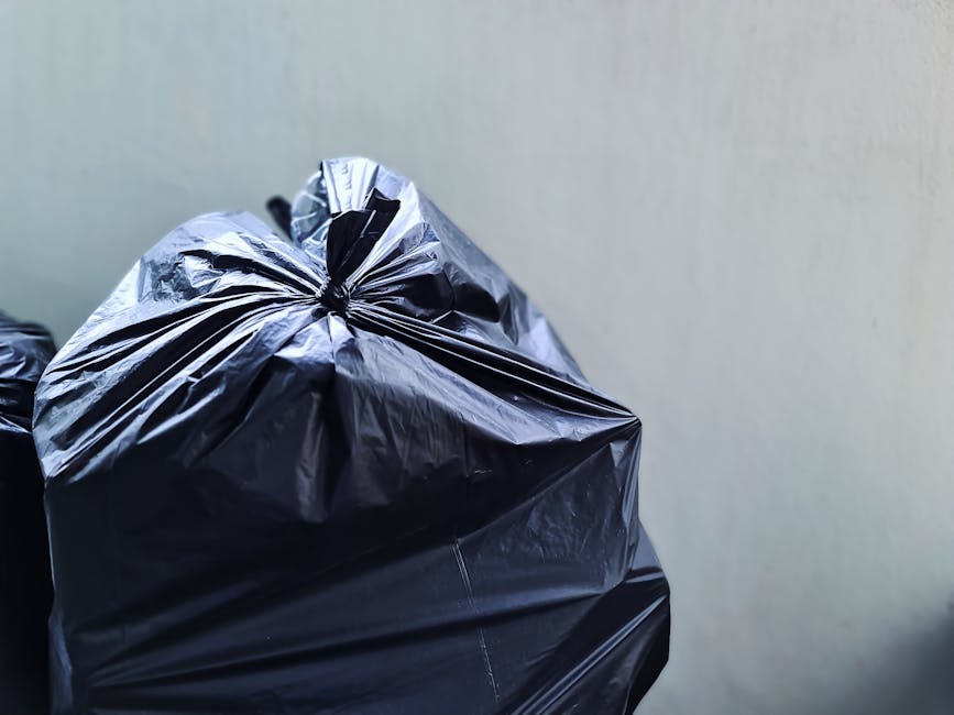 A person wearing a white shirt and beige trousers is holding a clear plastic bag, preparing to dispose of metal waste. They are standing near a white bin labeled 'METAL' with black uppercase letters,